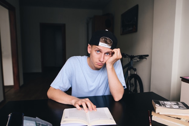 Joven con una triste expresión facial lee un libro en su casa.