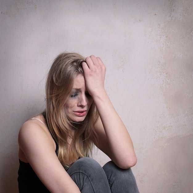Una joven triste sentada junto a la pared en casa.