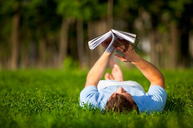 Joven tumbado en la hierba verde y libro de lectura