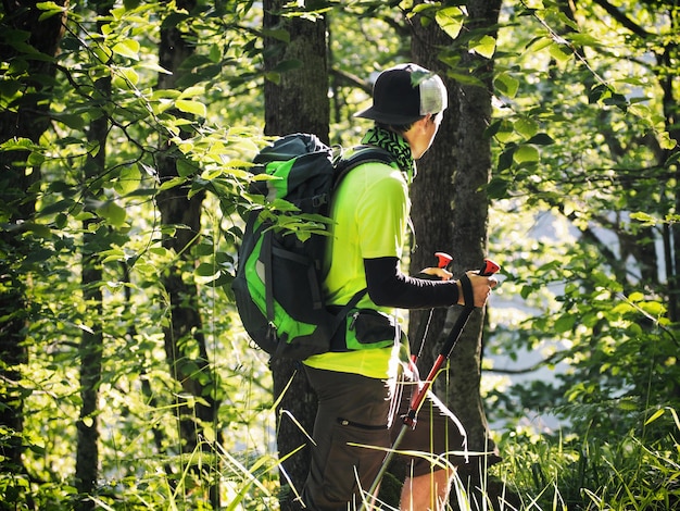 Joven turista activo con mochila y bastones de trekking en el bosque