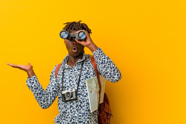 Joven turista africano hombre de pie contra un fondo amarillo sosteniendo un binoculares