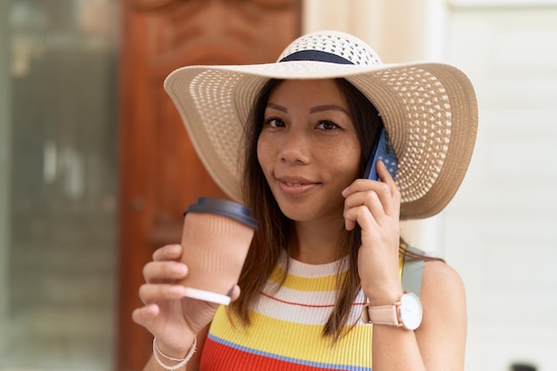 Joven turista asiática hablando por teléfono inteligente tomando café en la calle