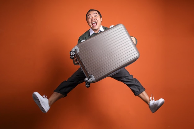 Joven turista asiático feliz saltando con equipaje listo para viajar aislado en fondo naranja