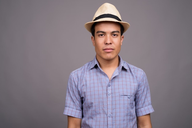 Joven turista asiático con sombrero listo para vacaciones contra la pared gris