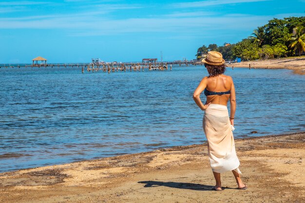 Un joven turista en bikini y falda en la playa de Sandy Bay en la isla de Roatán mirando el mar Caribe. Honduras