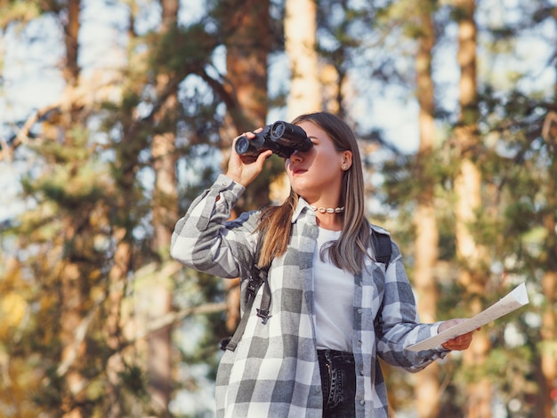 Un joven turista camina por el bosque mirando a lo lejos a través de binoculares.