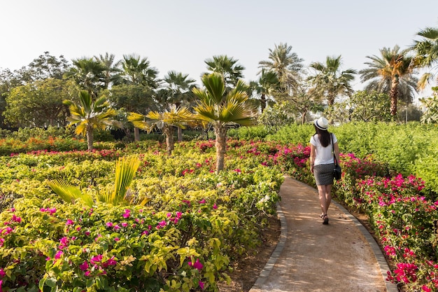 Una joven turista caucásica con un sombrero blanco camina en un jardín botánico con plantas exóticas