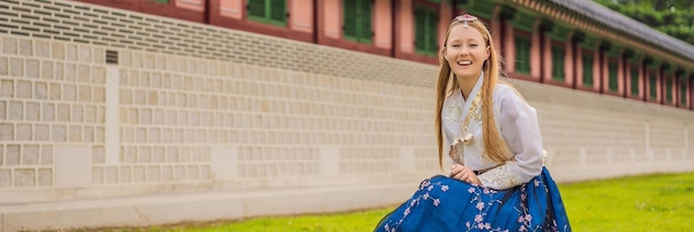 Joven turista caucásica con vestido nacional coreano hanbok Concepto de viaje a Corea Ropa nacional coreana Entretenimiento para turistas probándose ropa nacional coreana BANNER FORMATO LARGO