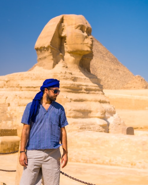 Un joven turista cerca de la gran esfinge de giza vestido de azul y un turbante azul, de donde se encuentran las miramides de giza, turismo cultural y mucha historia. el cairo, egipto