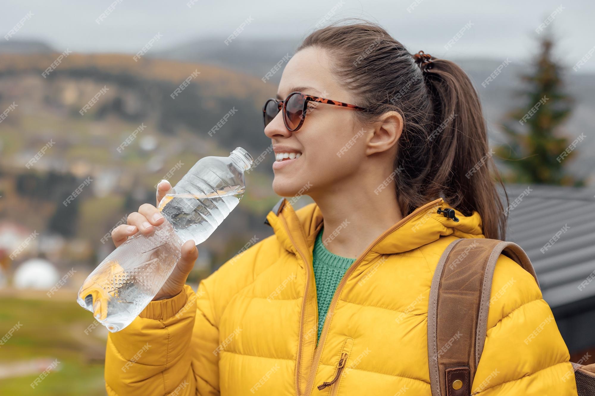 Joven turista con amarilla bebe agua fresca en la naturaleza el fondo de las montañas | Foto Premium