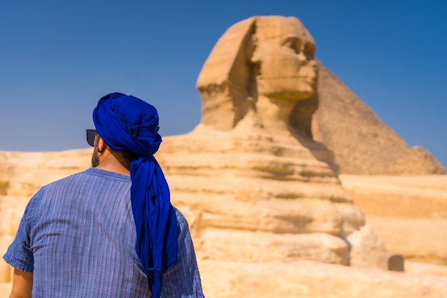 Un joven turista disfrutando y admirando la Gran Esfinge de Giza vestida de azul y un turbante azul. El Cairo, Egipto