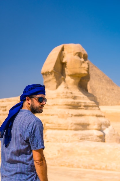 Un joven turista disfrutando y admirando la Gran Esfinge de Giza vestida de azul y un turbante azul. El Cairo, Egipto