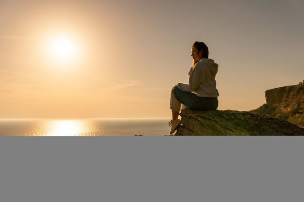 Foto una joven turista disfrutando de la puesta de sol sobre el mar paisaje de montaña mientras está sentado yoga para mujeres al aire libre