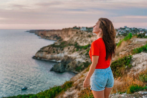 Una joven turista se encuentra en la orilla muy por encima del mar al atardecer y admira Cape Fiolent