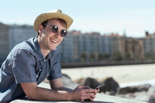 Joven turista feliz y sonriente revisando su teléfono en la costa de una ciudad.