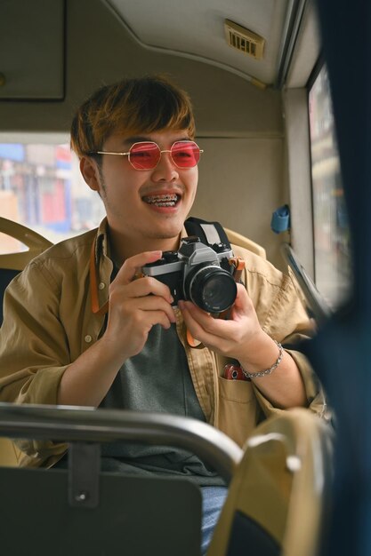 Foto joven turista con gafas rosadas con cámara disfrutando del viaje en autobús