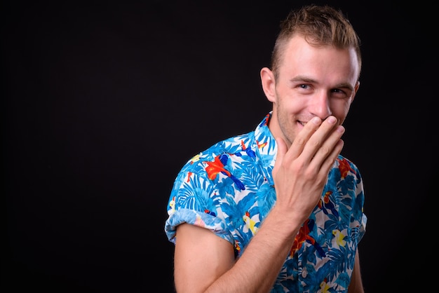 Joven turista guapo con cabello rubio listo para vacaciones contra la pared negra