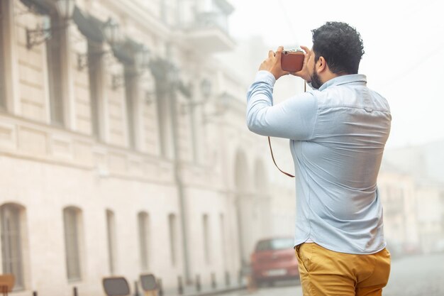 Joven turista hispano barbudo con una cámara retro en la ciudad Concepto de viaje