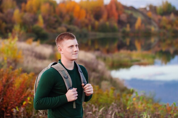 Joven turista con mochila cerca del lago de otoño