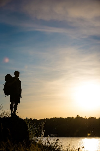 Joven turista con mochila de pie sobre una roca y disfrutando del atardecer