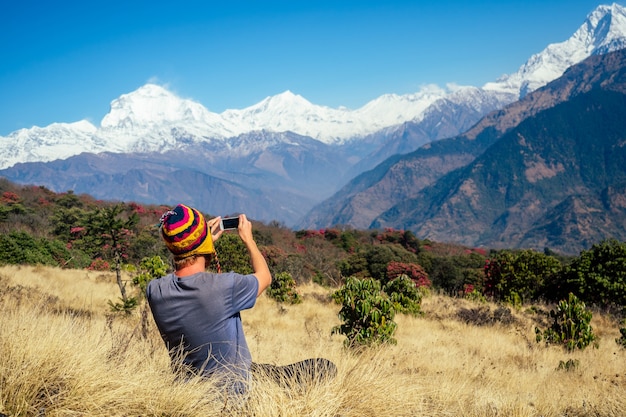 Un joven turista con una mochila de senderismo y un gorro tejido tomando fotografías de los paisajes y haciendo selfi en las montañas del Himalaya. concepto de trekking en las montañas.