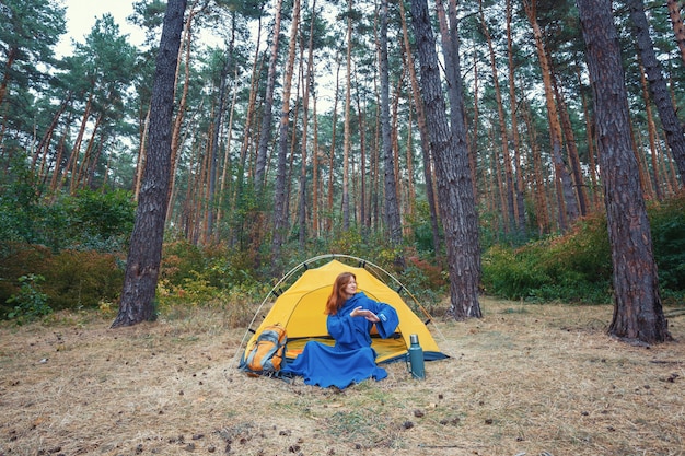 Joven turista niña bonita en bata azul haciendo ejercicios después de despertarse en el bosque