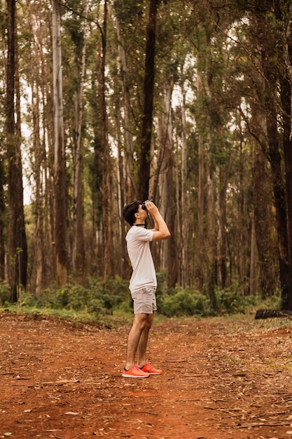 Foto joven turista observando árboles con binoculares. caminante en la selva mirando a su alrededor.