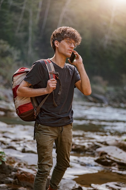 Joven turista perdido con mochila vagando por el río en las montañas y hablando por celular