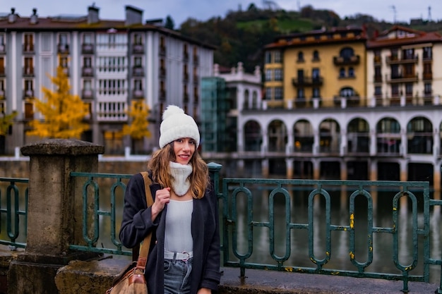 Una joven turista posa con su gorra y mochila al lado de una barandilla Es frío y es otoño