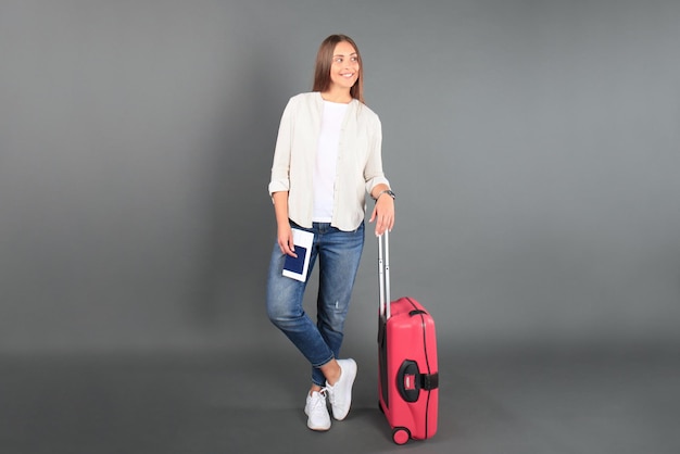 Joven turista con ropa informal de verano, con gafas de sol, maleta roja, pasaporte, entradas aisladas de fondo gris.