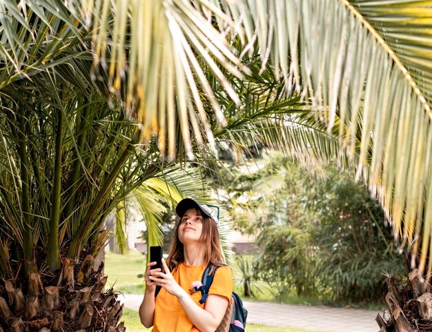 Foto una joven turista sonriente con gorra tomando una foto con su teléfono inteligente de cicas de palmeras tropicales