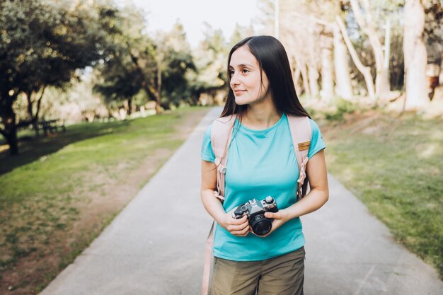 Joven turista viajera, con camiseta turquesa y mochila, tomando fotos en el parque