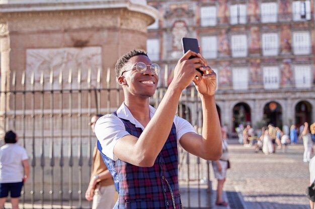 Joven turista visitando la plaza mayor de madrid transmitiendo su viaje en su teléfono móvil