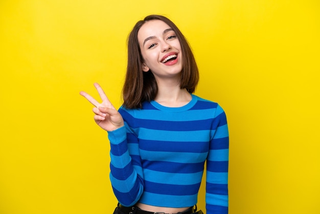 Joven ucraniana aislada de fondo amarillo sonriendo y mostrando el signo de la victoria