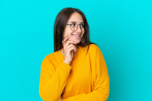 Joven ucraniana aislada de fondo azul con gafas y pensando mientras mira hacia arriba