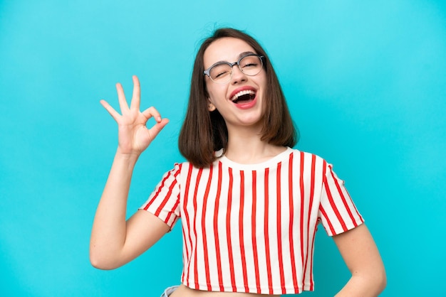 Joven ucraniana aislada de fondo azul que muestra el signo de ok con los dedos