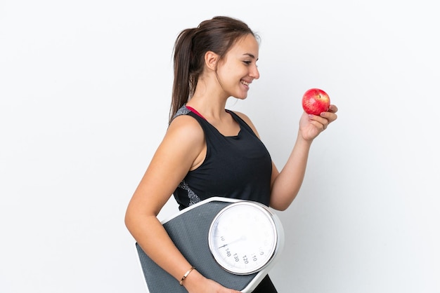 Joven ucraniana aislada de fondo blanco con máquina de pesaje y con una manzana