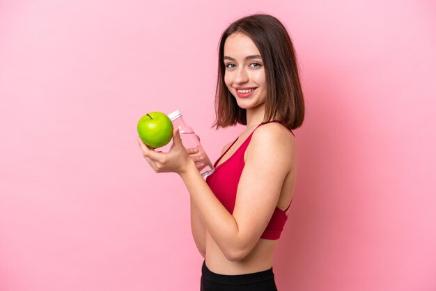 Joven ucraniana aislada de fondo rosa con una manzana y una botella de agua