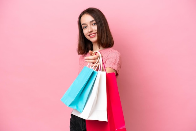 Joven ucraniana aislada de fondo rosa sosteniendo bolsas de compras y dándoselas a alguien