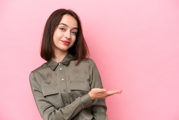 Foto una joven ucraniana aislada sobre un fondo rosado presenta una idea mientras mira sonriendo hacia