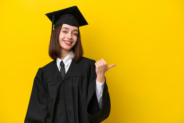 Joven ucraniana graduada de la universidad aislada de fondo amarillo apuntando hacia un lado para presentar un producto