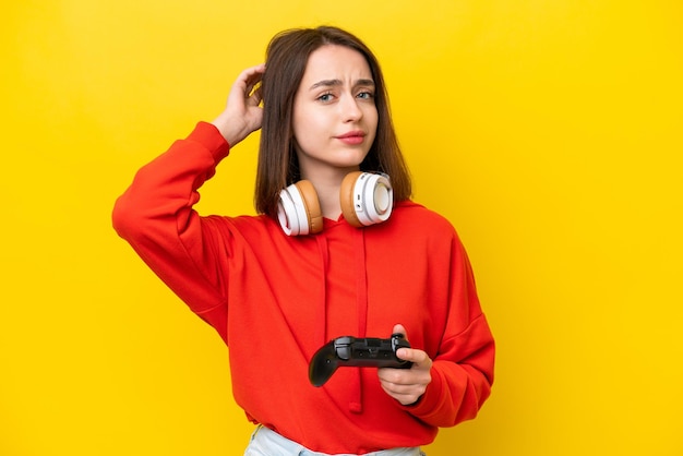 Joven ucraniana jugando con un controlador de videojuegos aislado en un fondo amarillo que tiene dudas