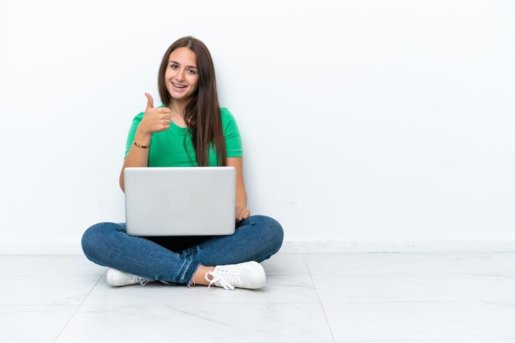 Foto joven ucraniana con una laptop sentada en el piso dando un gesto de aprobación