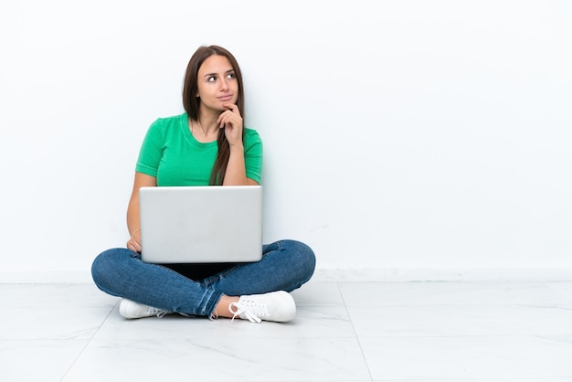 Joven ucraniana con una laptop sentada en el piso y mirando hacia arriba