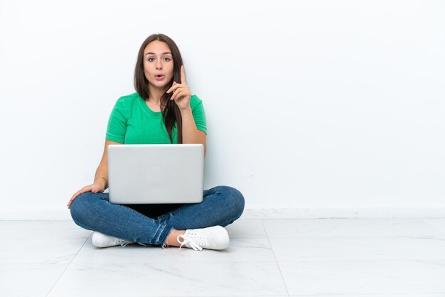 Foto joven ucraniana con una laptop sentada en el suelo con la intención de darse cuenta de la solución mientras levanta un dedo