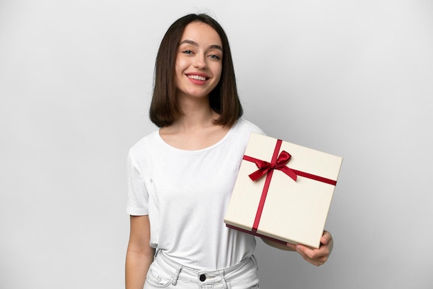 Joven ucraniana sosteniendo un regalo aislado de fondo blanco sonriendo mucho