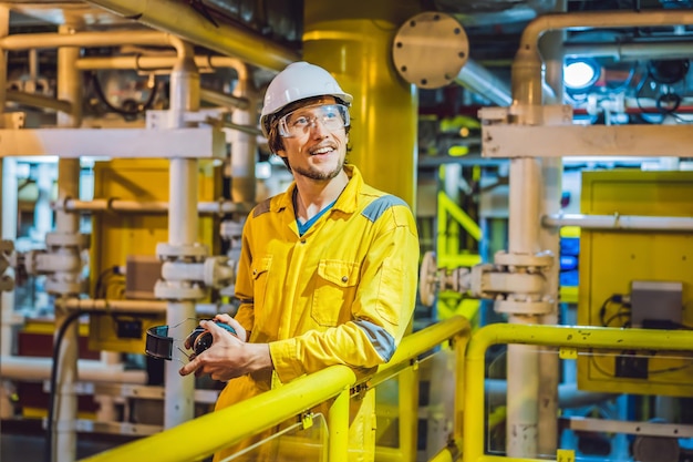 Joven con uniforme de trabajo amarillo, gafas y casco en una plataforma de aceite ambiental industrial o