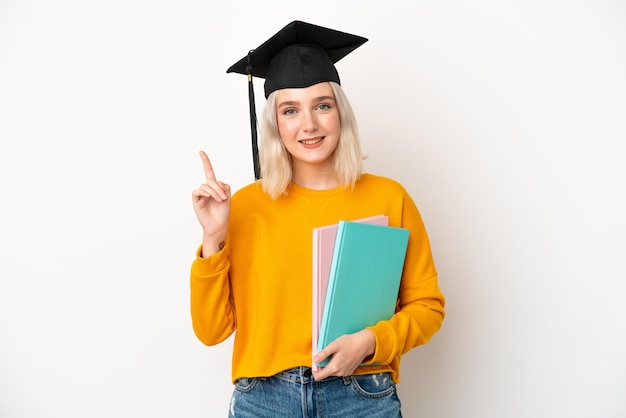 Joven universitaria caucásica graduada aislada de fondo blanco mostrando y levantando un dedo en señal de lo mejor