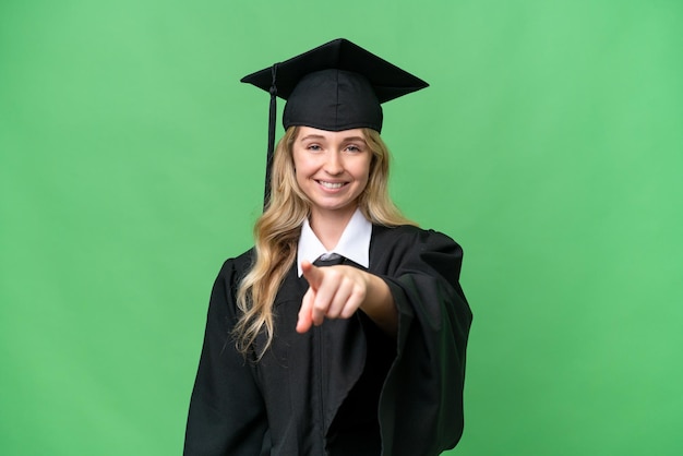 Una joven universitaria graduada en inglés sobre un fondo aislado te señala con una expresión de confianza