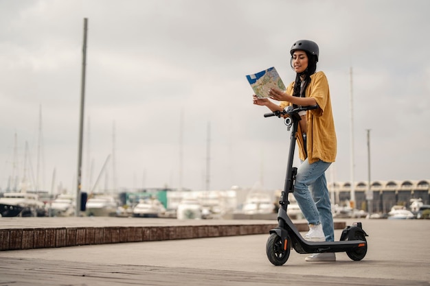 Una joven urbana está de pie con su paseo ecológico y mirando el mapa de la ciudad